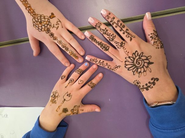 Three hands adorned with intricate henna designs on a purple surface.