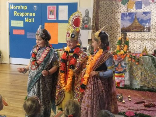 Three children dressed in traditional attire perform on stage, surrounded by festive decorations.