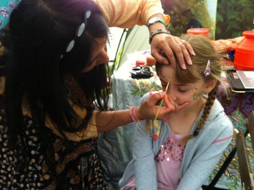 A BHS teacher applying face paint to a young girl during a Diwali workshop.