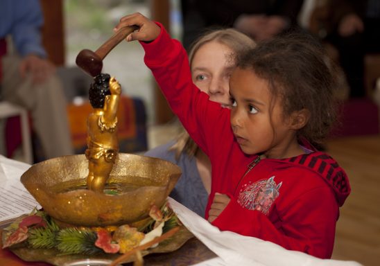 A child holding a wooden ladle above a sbathing bowl during a cuLtural event.
