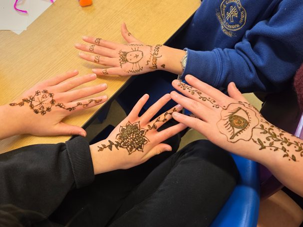 Four hands decorated with intricate henna designs on a table.