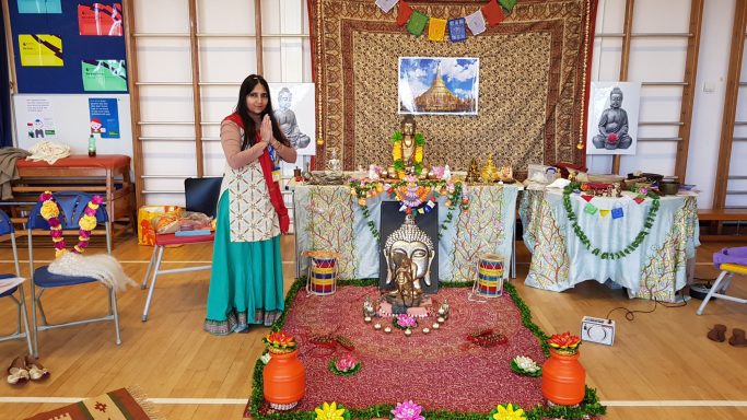 A woman in traditional attire performs a ritual in a decorated hall with floral arrangements.